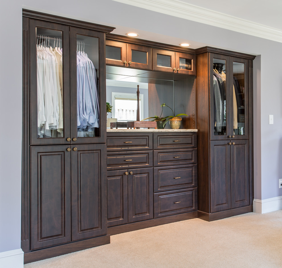 Inspiration for a mid-sized traditional men's dressing room in Raleigh with raised-panel cabinets, dark wood cabinets and carpet.