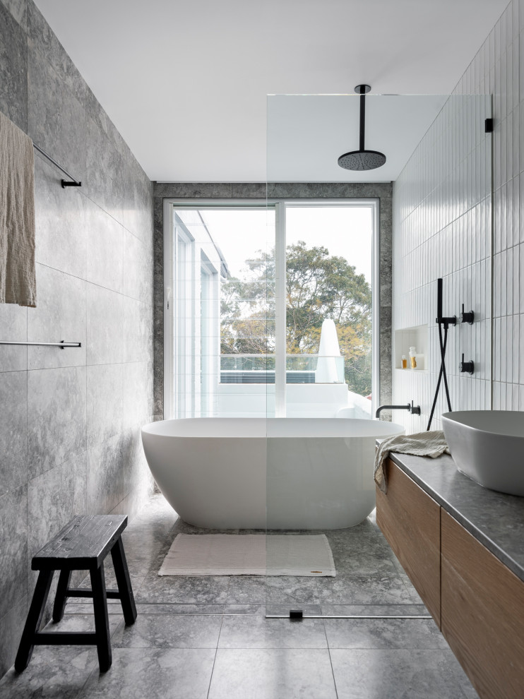 Inredning av ett modernt stort badrum, med skåp i ljust trä, ett fristående badkar, en öppen dusch, tunnelbanekakel, kalkstensgolv och bänkskiva i kalksten