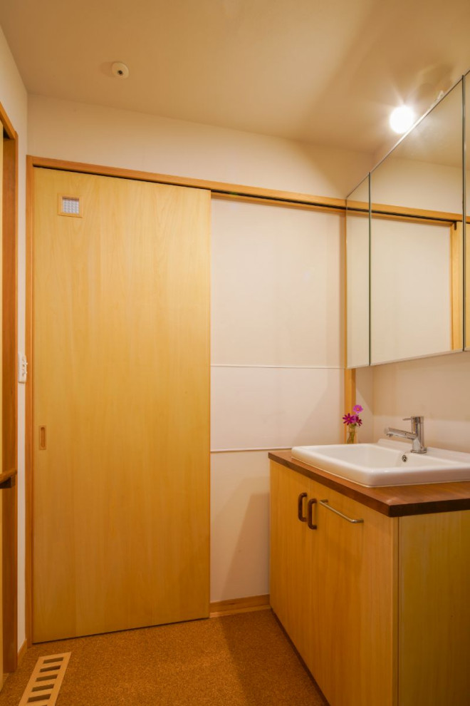 Photo of a small arts and crafts powder room in Other with flat-panel cabinets, beige cabinets, white walls, cork floors, an undermount sink, wood benchtops, brown floor, brown benchtops and a built-in vanity.