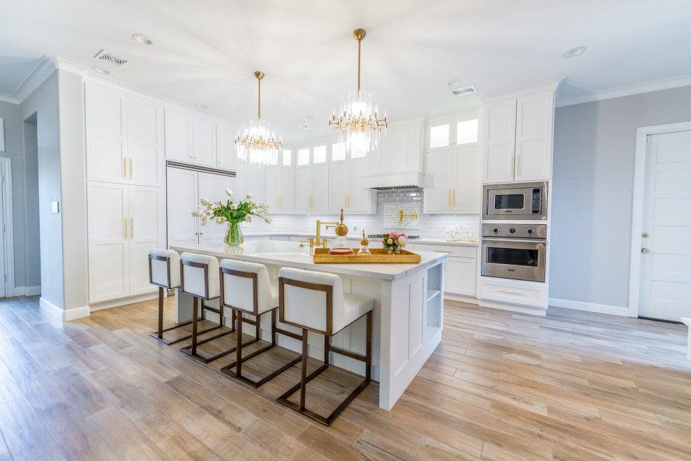 Large modern l-shaped eat-in kitchen in Houston with an undermount sink, shaker cabinets, white cabinets, white splashback, subway tile splashback, panelled appliances, vinyl floors, with island, brown floor and vaulted.