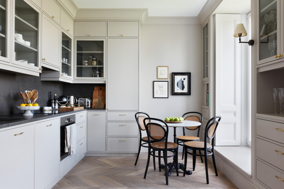 Inspiration for a transitional l-shaped eat-in kitchen in London with flat-panel cabinets, grey splashback, stainless steel appliances, medium hardwood floors, no island, brown floor, grey benchtop and grey cabinets.
