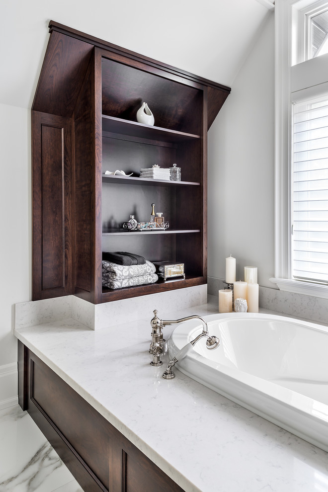 This is an example of a large transitional master bathroom in Toronto with recessed-panel cabinets, dark wood cabinets, a drop-in tub, white tile, marble floors, quartzite benchtops, a one-piece toilet, porcelain tile and white walls.