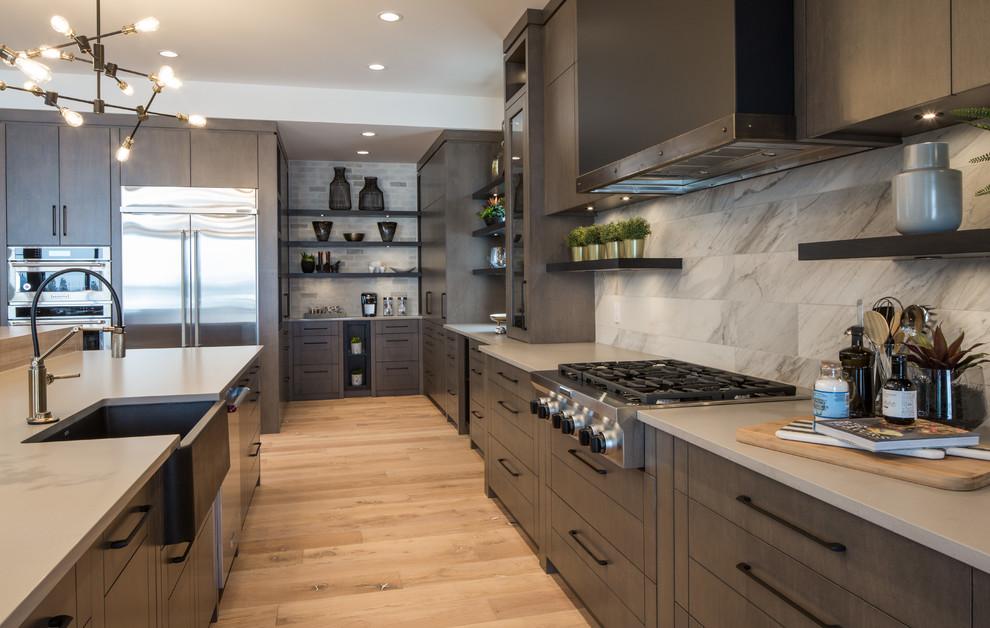 Inspiration for an expansive contemporary l-shaped eat-in kitchen in Calgary with a farmhouse sink, flat-panel cabinets, dark wood cabinets, quartz benchtops, white splashback, ceramic splashback, stainless steel appliances, medium hardwood floors, with island, brown floor and grey benchtop.