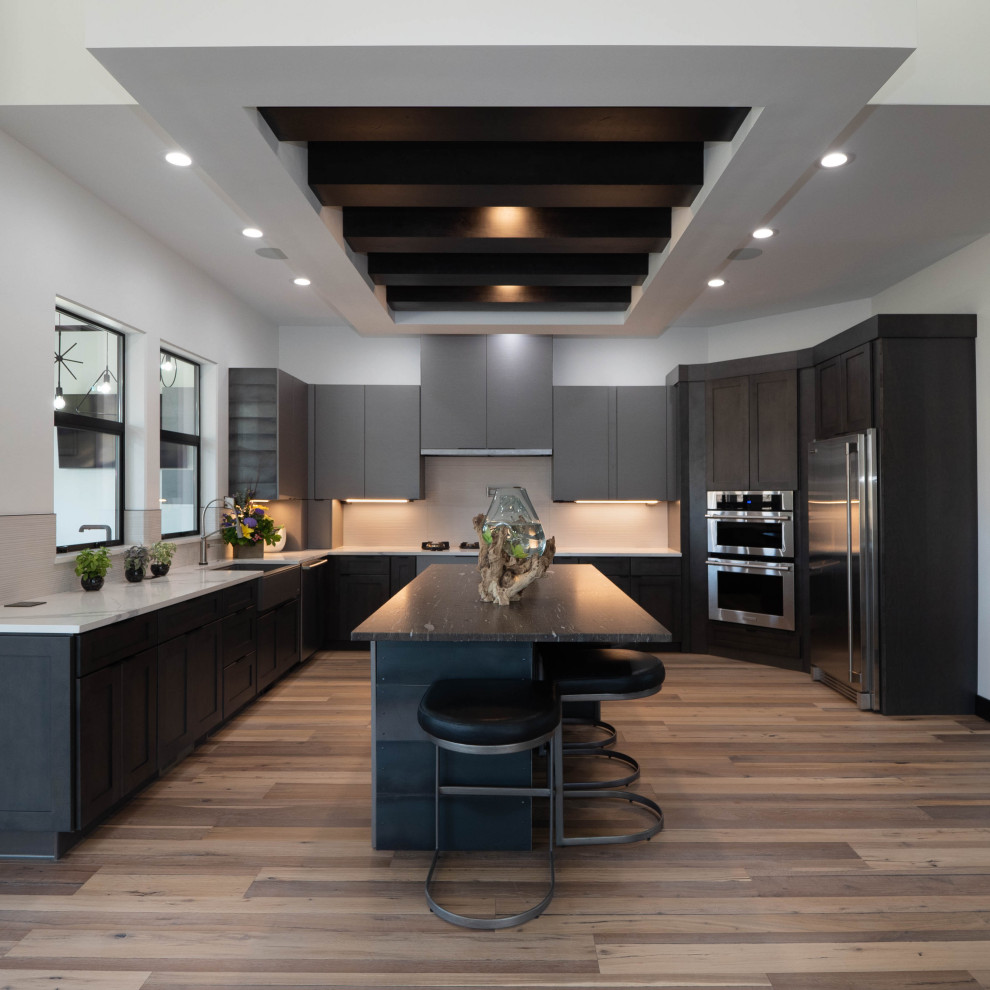 Photo of an expansive contemporary u-shaped kitchen in Denver with a farmhouse sink, shaker cabinets, dark wood cabinets, beige splashback, stainless steel appliances, medium hardwood floors, with island, brown floor and white benchtop.
