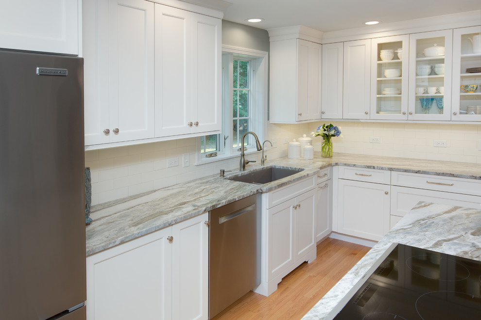 Transitional l-shaped light wood floor eat-in kitchen photo in Boston with an undermount sink, recessed-panel cabinets, white cabinets, quartzite countertops, white backsplash, subway tile backsplash, stainless steel appliances and an island