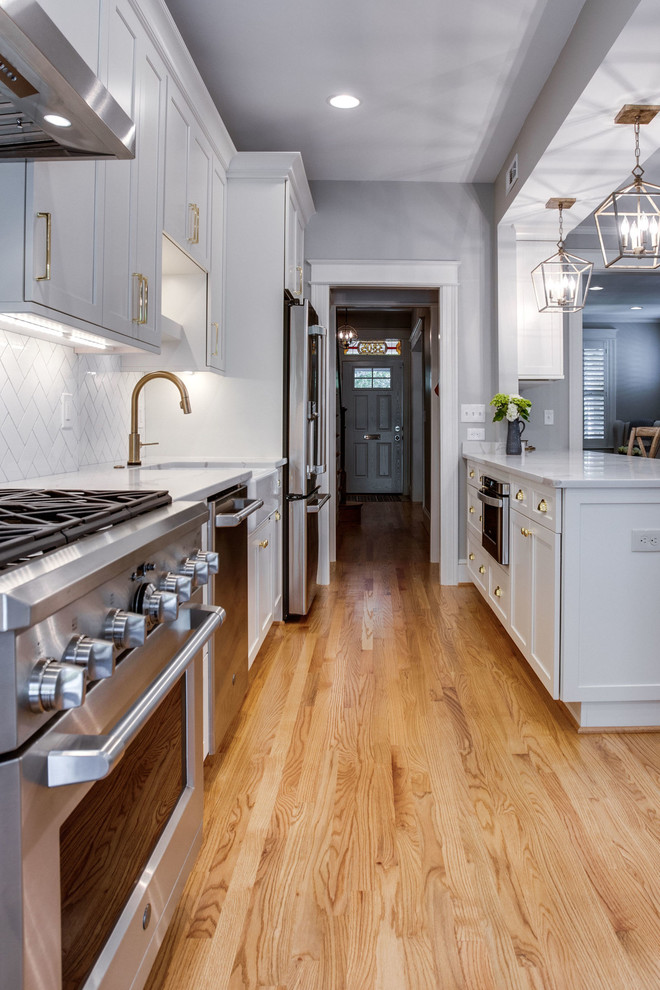 Example of a mid-sized transitional galley light wood floor and beige floor eat-in kitchen design in DC Metro with a farmhouse sink, shaker cabinets, white cabinets, quartz countertops, white backsplash, subway tile backsplash, stainless steel appliances, a peninsula and white countertops