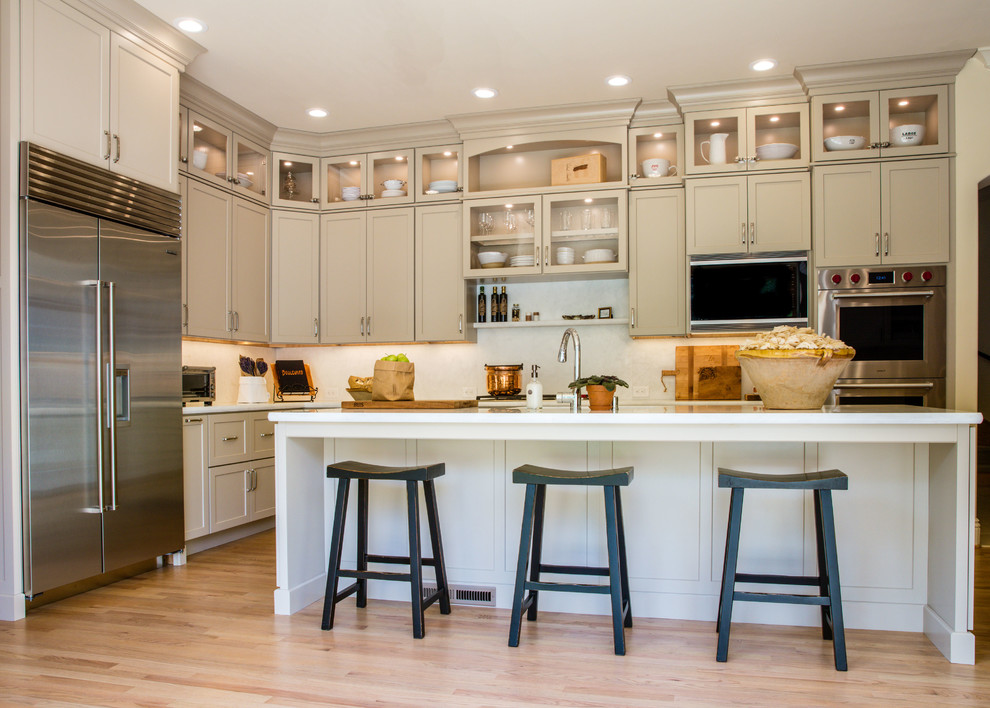 Mid-sized traditional l-shaped eat-in kitchen in San Francisco with a single-bowl sink, recessed-panel cabinets, beige cabinets, marble benchtops, beige splashback, porcelain splashback, stainless steel appliances, light hardwood floors, with island and beige floor.