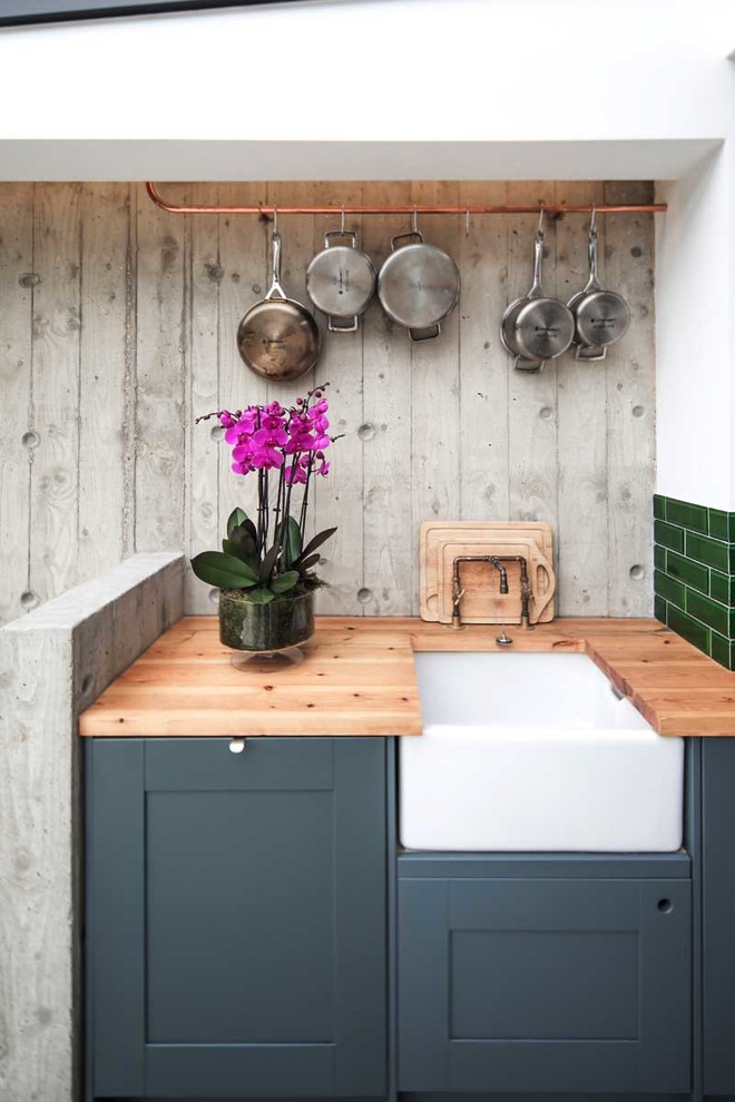 Small contemporary open plan kitchen in Sussex with a farmhouse sink, shaker cabinets, grey cabinets, wood benchtops, green splashback, subway tile splashback, stainless steel appliances, concrete floors, a peninsula, grey floor and grey benchtop.