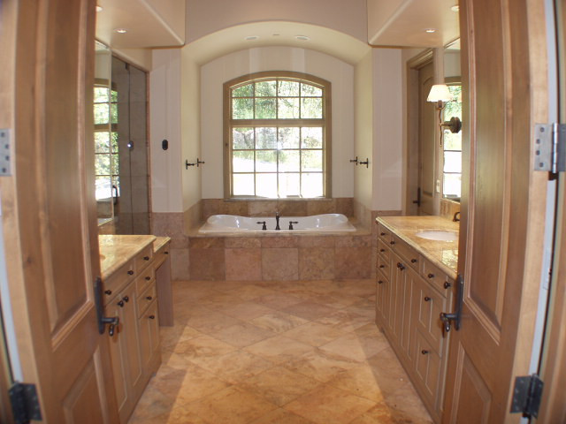 Design ideas for a mid-sized country master bathroom in Austin with recessed-panel cabinets, medium wood cabinets, a drop-in tub, an alcove shower, a two-piece toilet, beige tile, limestone, beige walls, travertine floors, an undermount sink, limestone benchtops, beige floor, a hinged shower door and beige benchtops.