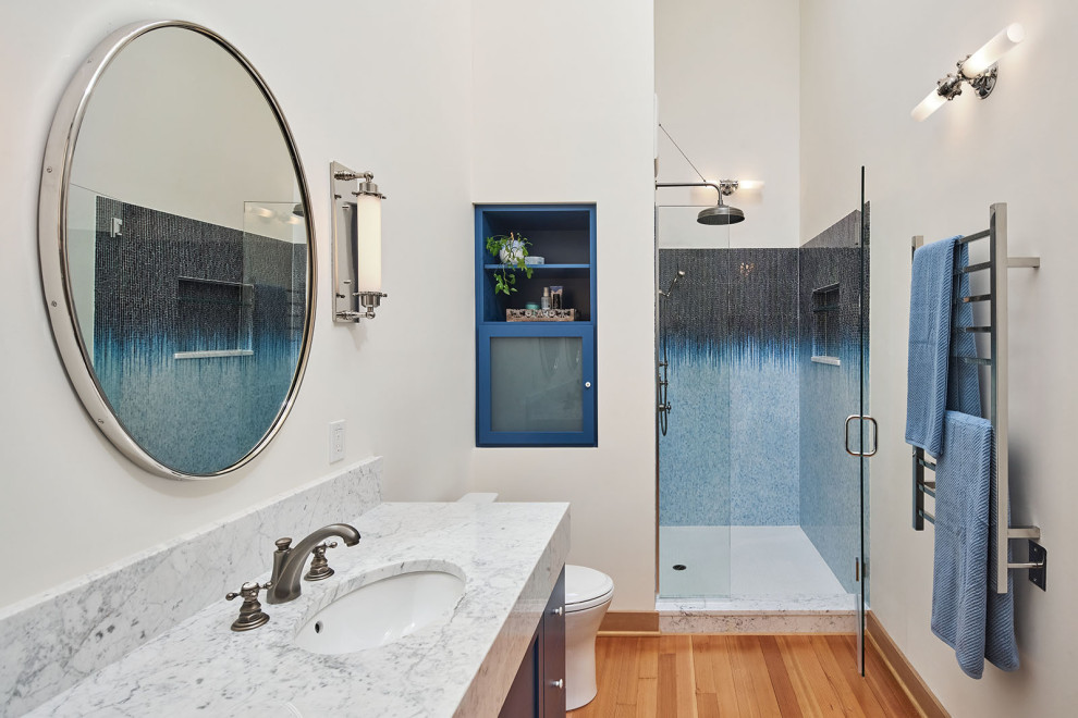 Design ideas for a mid-sized industrial master bathroom in Portland with recessed-panel cabinets, blue cabinets, an alcove shower, a one-piece toilet, white walls, medium hardwood floors, an undermount sink, marble benchtops, brown floor, a hinged shower door, multi-coloured benchtops, a niche, a double vanity and exposed beam.