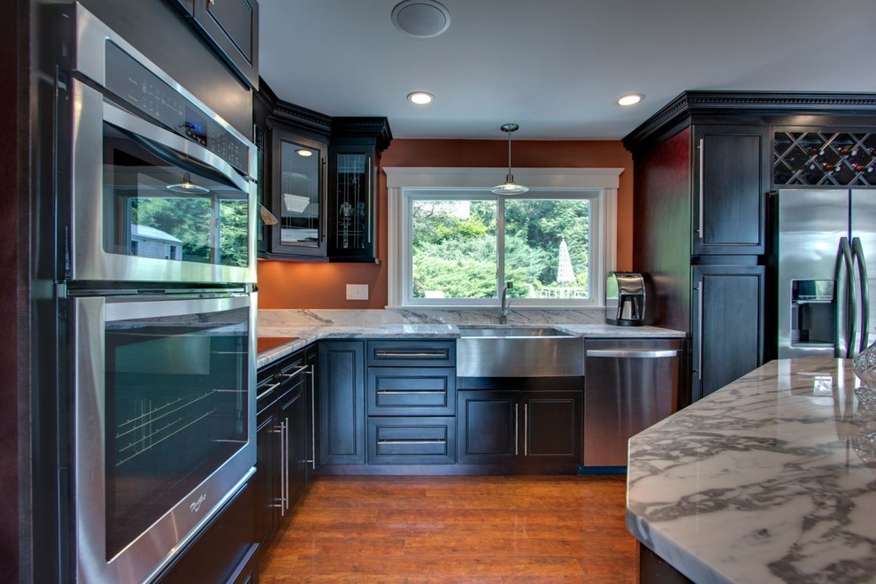 Inspiration for a mid-sized transitional l-shaped medium tone wood floor and brown floor eat-in kitchen remodel in Raleigh with a farmhouse sink, raised-panel cabinets, dark wood cabinets, marble countertops, stainless steel appliances, an island and white countertops