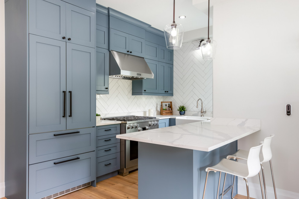 Photo of an expansive transitional l-shaped eat-in kitchen in Vancouver with an integrated sink, louvered cabinets, blue cabinets, quartz benchtops, white splashback, stone tile splashback, stainless steel appliances, light hardwood floors, with island, beige floor, white benchtop and wood.