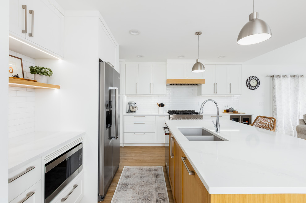 Mid-sized transitional l-shaped light wood floor and beige floor eat-in kitchen photo in Vancouver with an undermount sink, shaker cabinets, white cabinets, quartzite countertops, white backsplash, subway tile backsplash, stainless steel appliances, an island and white countertops