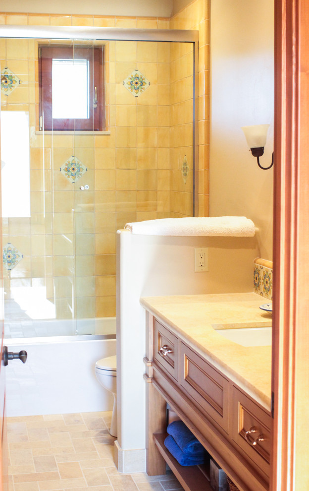 This is an example of a mid-sized mediterranean master bathroom in San Francisco with shaker cabinets, medium wood cabinets, an alcove tub, a shower/bathtub combo, a two-piece toilet, beige tile, stone tile, beige walls, medium hardwood floors, an undermount sink, granite benchtops, brown floor and a sliding shower screen.