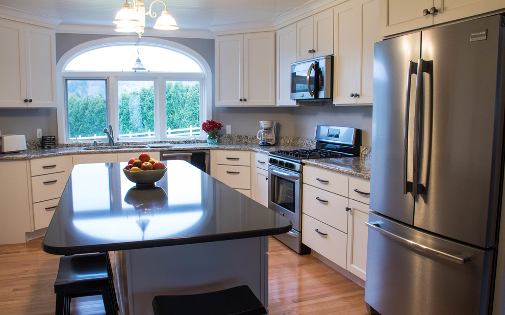 Mid-sized transitional u-shaped medium tone wood floor enclosed kitchen photo with an undermount sink, recessed-panel cabinets, white cabinets, quartz countertops, stainless steel appliances and an island