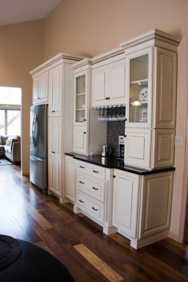 Eat-in kitchen - large transitional l-shaped medium tone wood floor eat-in kitchen idea with an undermount sink, raised-panel cabinets, distressed cabinets, granite countertops, black backsplash, stainless steel appliances and an island