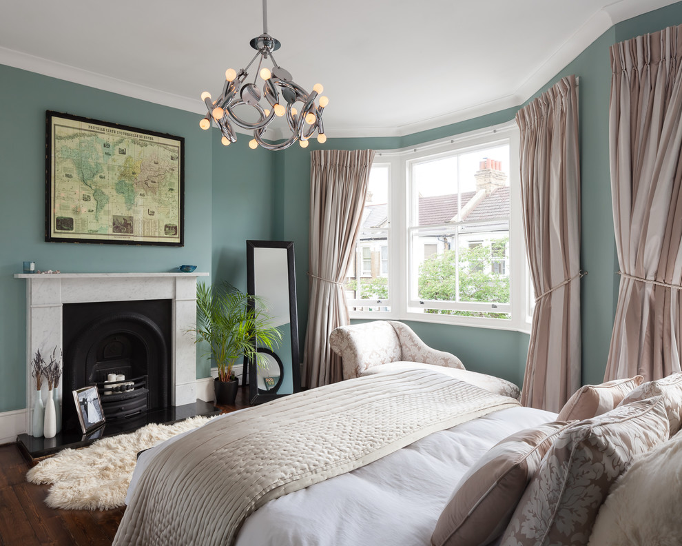 Photo of a large traditional master bedroom in London with green walls, dark hardwood floors, a standard fireplace, a stone fireplace surround and brown floor.