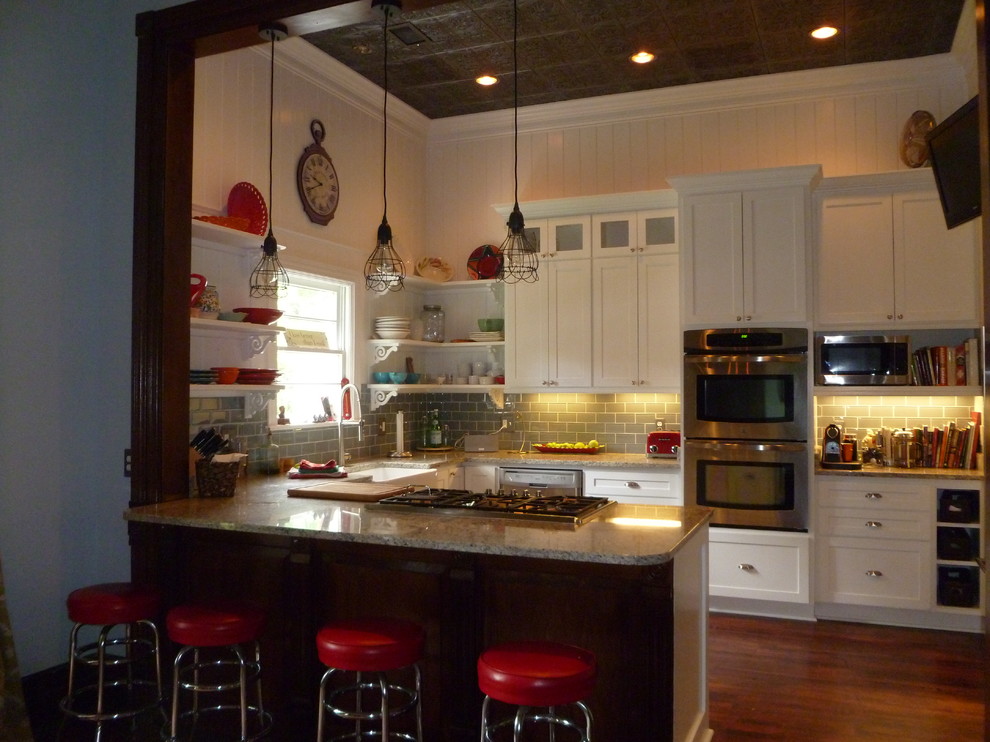 Small eclectic u-shaped eat-in kitchen in Nashville with a farmhouse sink, recessed-panel cabinets, white cabinets, granite benchtops, blue splashback, glass tile splashback, stainless steel appliances, medium hardwood floors and a peninsula.