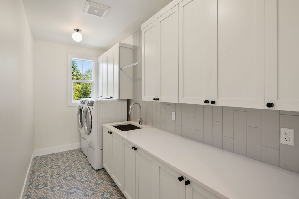 Inspiration for a medium sized single-wall separated utility room in Seattle with a built-in sink, recessed-panel cabinets, white cabinets, engineered stone countertops, grey splashback, metro tiled splashback, white walls, ceramic flooring, a side by side washer and dryer, multi-coloured floors and white worktops.
