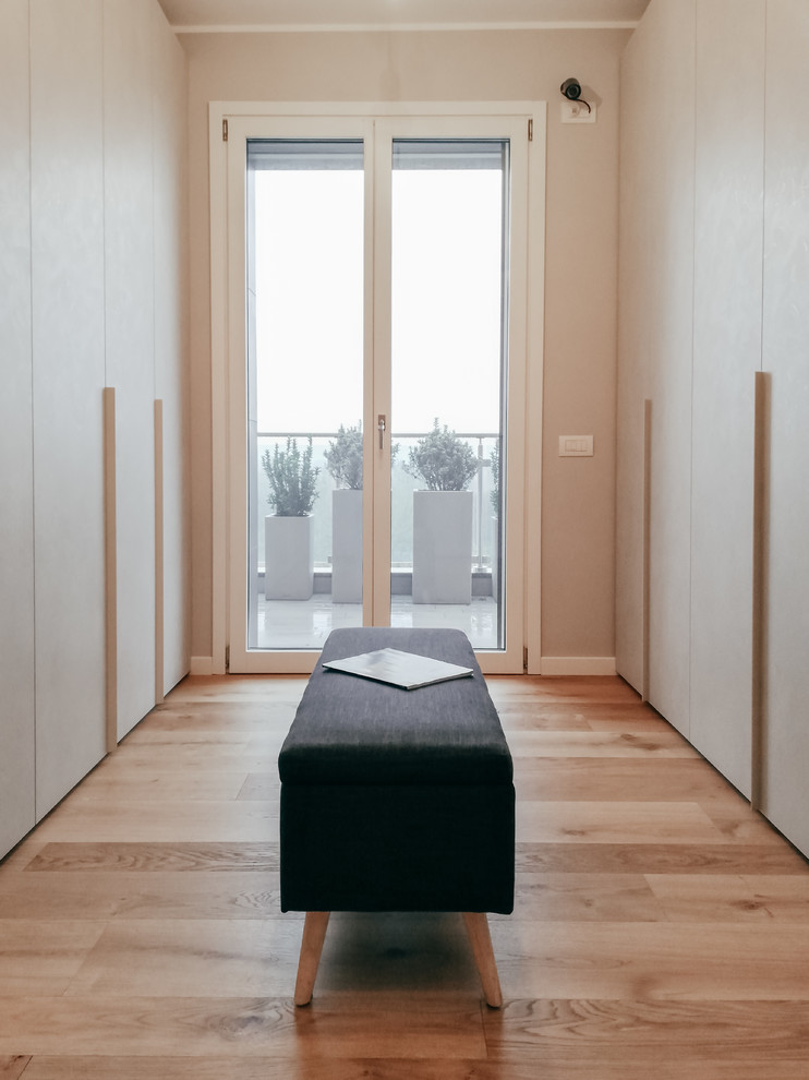 Photo of a large contemporary gender-neutral walk-in wardrobe in Milan with flat-panel cabinets and light hardwood floors.