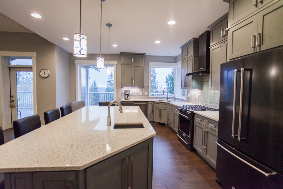 Large contemporary l-shaped open plan kitchen in Seattle with an undermount sink, shaker cabinets, grey cabinets, recycled glass benchtops, grey splashback, glass tile splashback, stainless steel appliances, with island, brown floor and dark hardwood floors.