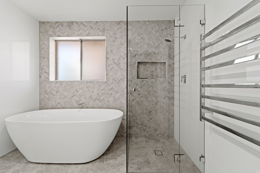 Design ideas for a mid-sized contemporary master bathroom with a freestanding tub, a corner shower, porcelain tile, grey walls, grey floor, a hinged shower door, a niche, a single vanity and decorative wall panelling.