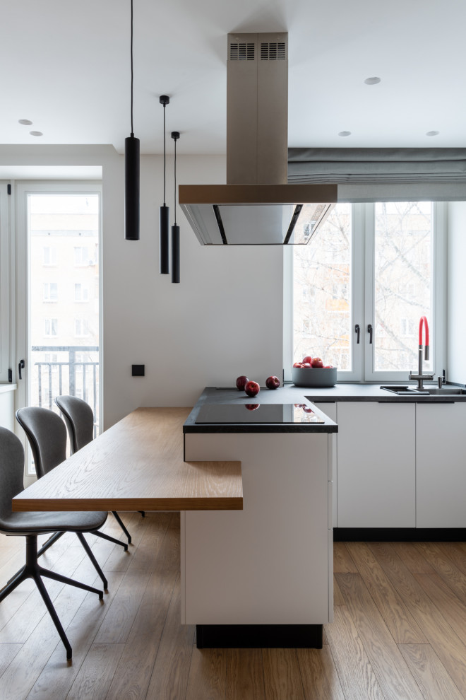 Свежая идея для дизайна: п-образная кухня-гостиная среднего размера в современном стиле с врезной мойкой, плоскими фасадами, белыми фасадами и паркетным полом среднего тона - отличное фото интерьера