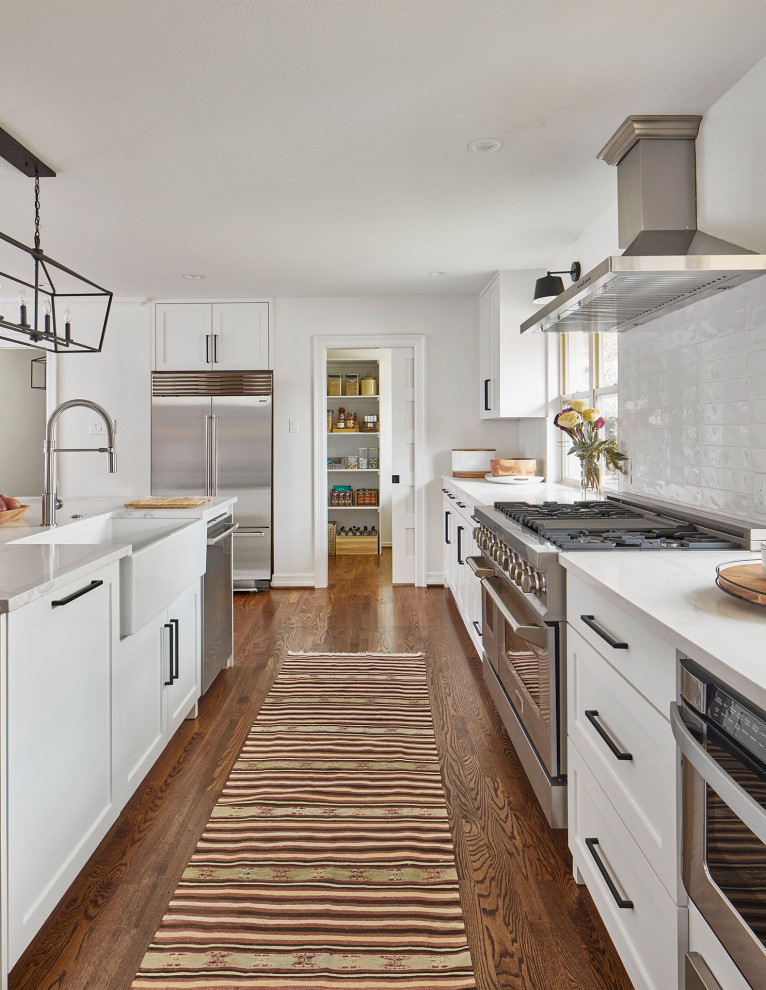Idéer för att renovera ett mellanstort vintage vit vitt kök, med en rustik diskho, skåp i shakerstil, vita skåp, bänkskiva i kvartsit, vitt stänkskydd, stänkskydd i stenkakel, rostfria vitvaror, mellanmörkt trägolv, en köksö och brunt golv