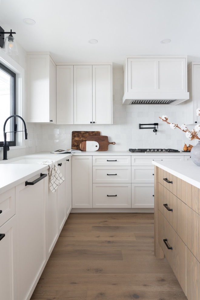 Mid-sized transitional u-shaped eat-in kitchen in Vancouver with a single-bowl sink, shaker cabinets, white cabinets, quartz benchtops, white splashback, porcelain splashback, stainless steel appliances, medium hardwood floors, with island and grey benchtop.