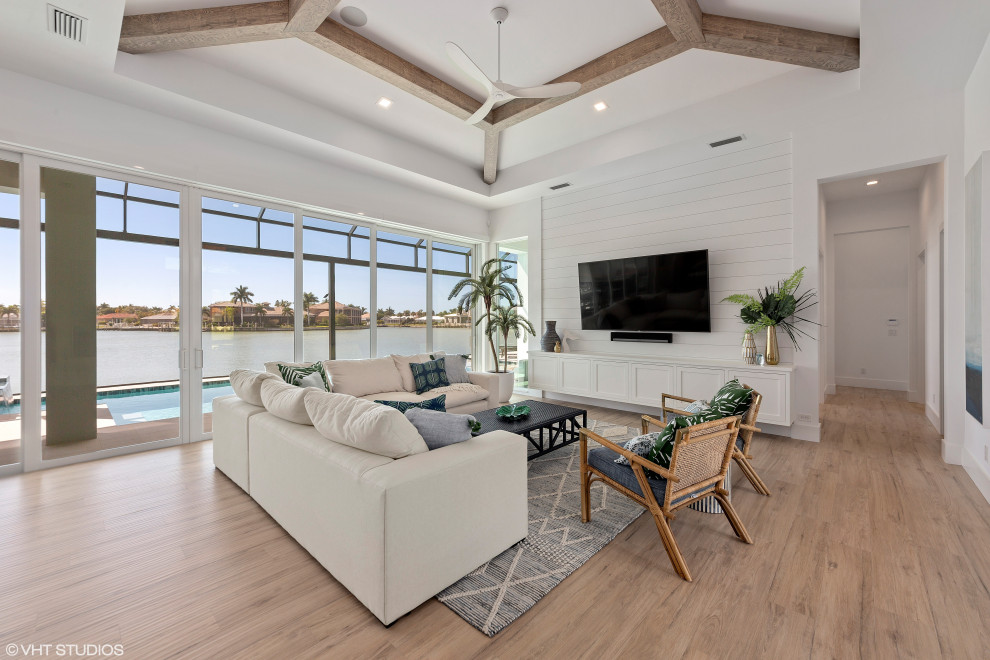 This is an example of a large beach style open concept living room in Tampa with white walls, porcelain floors, a wall-mounted tv and beige floor.