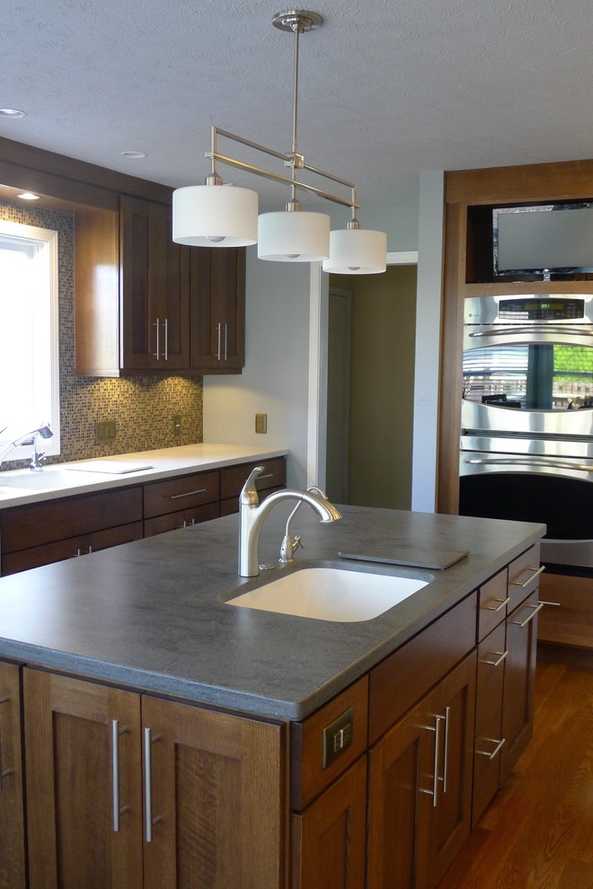Design ideas for a mid-sized transitional u-shaped eat-in kitchen in Indianapolis with an integrated sink, shaker cabinets, medium wood cabinets, solid surface benchtops, brown splashback, stainless steel appliances, medium hardwood floors and with island.