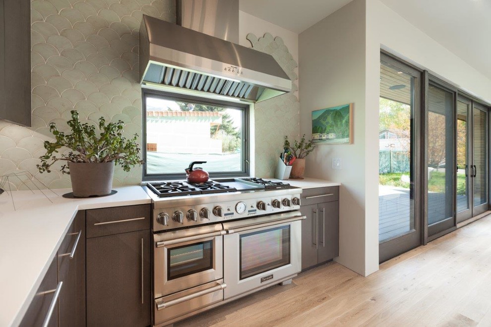 This is an example of a large modern u-shaped eat-in kitchen in Other with flat-panel cabinets, brown cabinets, blue splashback, stainless steel appliances, light hardwood floors, with island and brown floor.