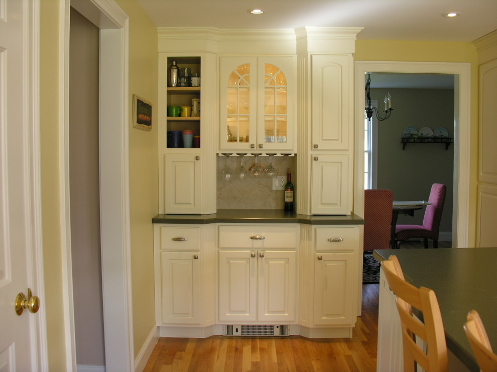 This is an example of a small traditional single-wall wet bar in Portland Maine with an undermount sink, raised-panel cabinets, white cabinets, laminate benchtops, light hardwood floors, beige splashback and ceramic splashback.