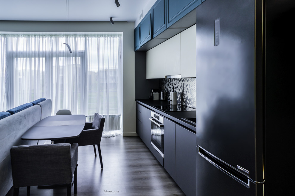 This is an example of a small transitional single-wall kitchen in Saint Petersburg with a drop-in sink, flat-panel cabinets, turquoise cabinets, metallic splashback, mirror splashback, stainless steel appliances, laminate floors, grey floor, black benchtop and recessed.