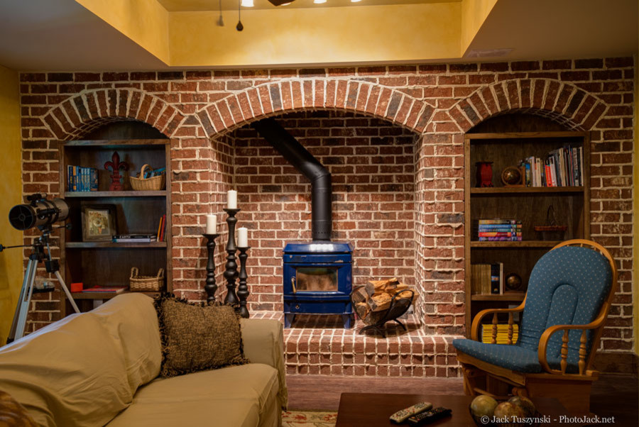 Photo of a large country fully buried basement in Atlanta with a wood stove, a brick fireplace surround, yellow walls and dark hardwood floors.