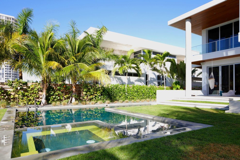 Design ideas for an expansive contemporary backyard l-shaped lap pool in Miami with a hot tub and concrete slab.