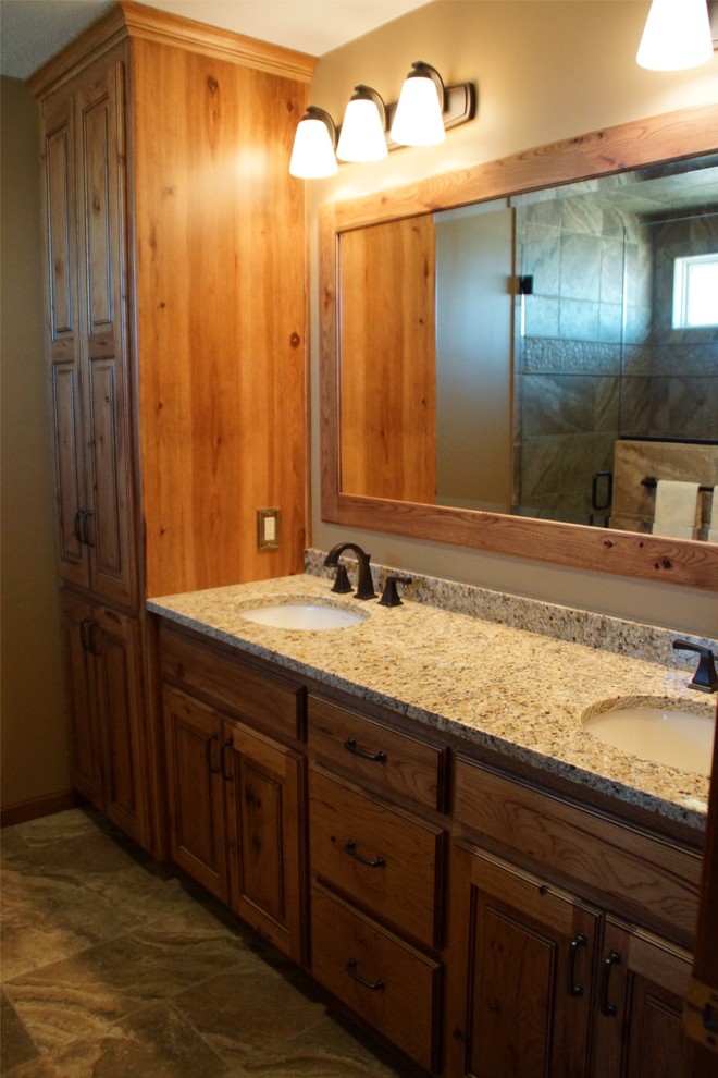 Alcove shower - mid-sized rustic master multicolored tile and stone tile travertine floor alcove shower idea with raised-panel cabinets, medium tone wood cabinets, a one-piece toilet, beige walls, an undermount sink and granite countertops