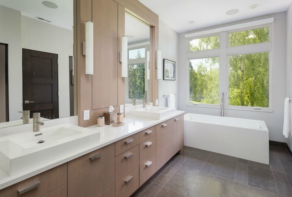 This is an example of a mid-sized contemporary master bathroom in Seattle with flat-panel cabinets, a freestanding tub, gray tile, porcelain tile, white walls, porcelain floors, quartzite benchtops, a vessel sink, light wood cabinets, an alcove shower and white benchtops.