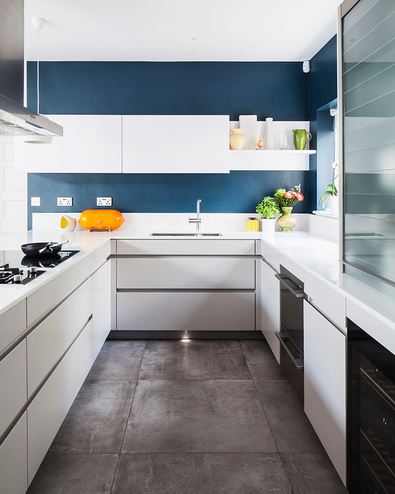 Inspiration for a large contemporary open plan kitchen in Sussex with a drop-in sink, flat-panel cabinets, white cabinets, laminate benchtops, metallic splashback, stainless steel appliances, concrete floors and a peninsula.