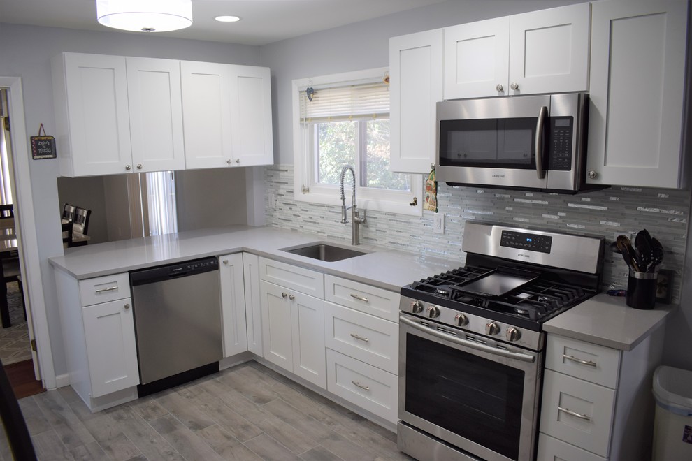 Large transitional l-shaped separate kitchen in Baltimore with an undermount sink, shaker cabinets, white cabinets, quartz benchtops, grey splashback, matchstick tile splashback, stainless steel appliances, light hardwood floors, no island, grey floor and white benchtop.