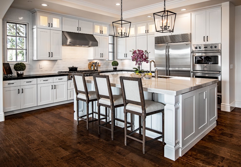 Example of a large transitional l-shaped dark wood floor and brown floor eat-in kitchen design in Orange County with an undermount sink, shaker cabinets, white cabinets, quartzite countertops, white backsplash, subway tile backsplash, stainless steel appliances, an island and white countertops