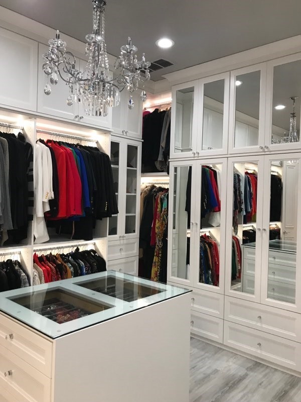 Large transitional gender-neutral walk-in wardrobe in Atlanta with glass-front cabinets, white cabinets and grey floor.