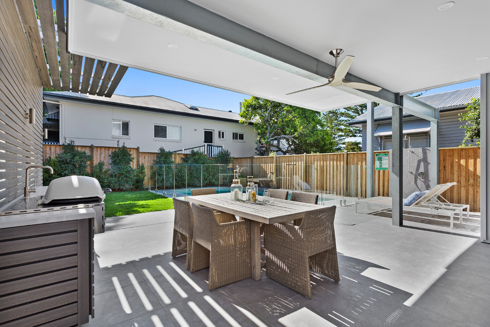 This is an example of a large contemporary backyard patio in Brisbane with an outdoor kitchen, a roof extension and tile.