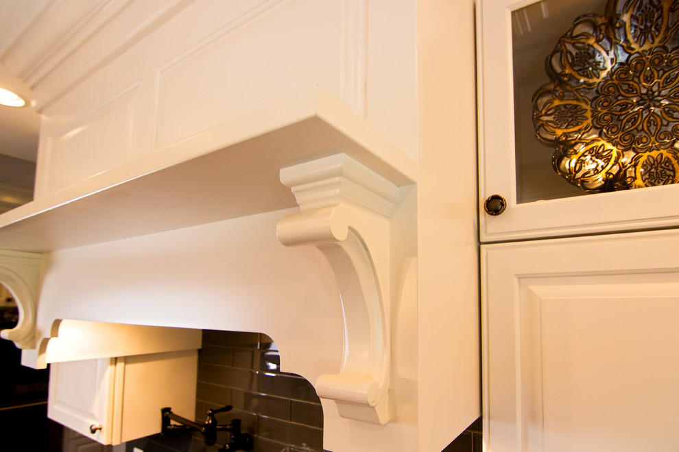 Kitchen - transitional l-shaped dark wood floor kitchen idea in Providence with a farmhouse sink, raised-panel cabinets, granite countertops, gray backsplash, glass tile backsplash, paneled appliances and an island