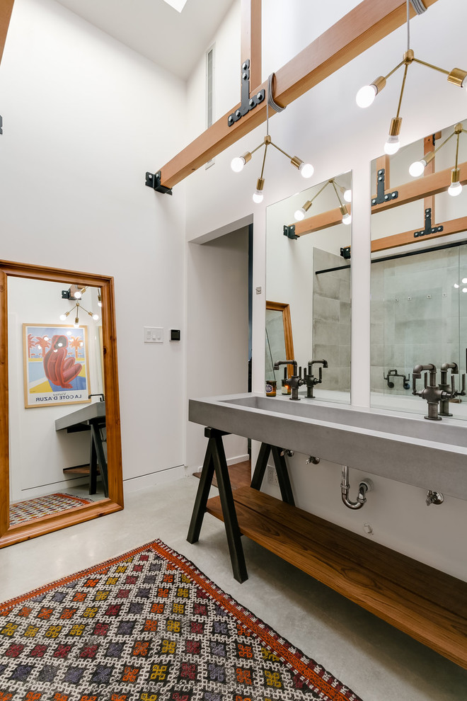 Photo of an industrial bathroom in Los Angeles with open cabinets, medium wood cabinets, white walls, a trough sink, grey floor, concrete benchtops and grey benchtops.