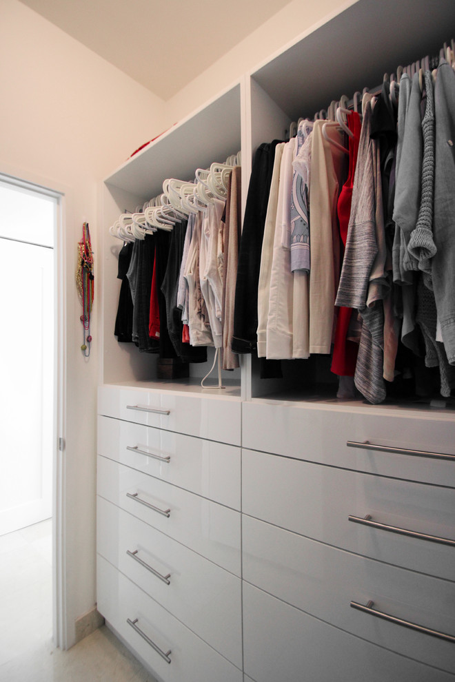 This is an example of a small contemporary gender-neutral walk-in wardrobe in Miami with flat-panel cabinets, white cabinets, porcelain floors and beige floor.