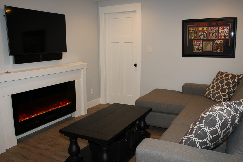 Imagen de sala de estar cerrada costera pequeña con paredes grises, suelo vinílico, chimenea lineal, marco de chimenea de madera y televisor colgado en la pared