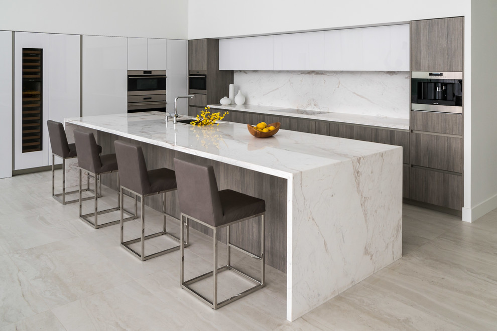 This is an example of a contemporary kitchen in Los Angeles with an undermount sink, flat-panel cabinets, white cabinets, white splashback, stone slab splashback, panelled appliances, with island, beige floor and white benchtop.