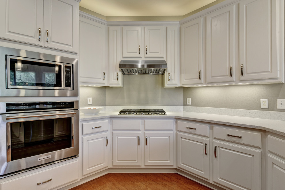Example of a mid-sized transitional u-shaped light wood floor eat-in kitchen design in Austin with an undermount sink, white cabinets, quartz countertops, white backsplash, stone slab backsplash, stainless steel appliances, a peninsula and raised-panel cabinets