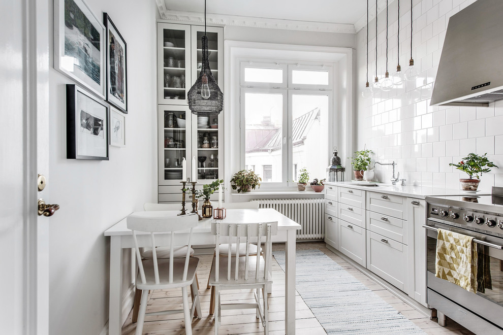 Scandinavian kitchen in Gothenburg with marble benchtops, white splashback, stainless steel appliances, light hardwood floors, no island, beige floor, shaker cabinets, white cabinets and subway tile splashback.